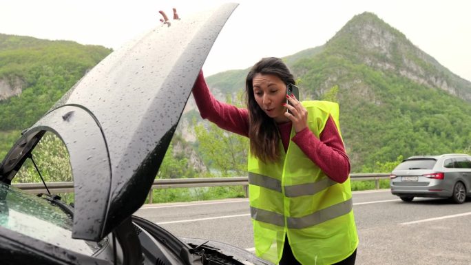 一名年轻女子在雨中呼叫道路救援，因为路上的汽车出了问题