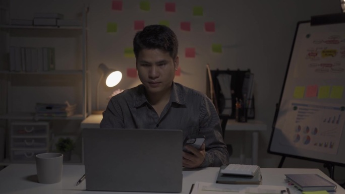 亚洲男性商人在办公室用财务文件和台式电脑工作到很晚，加班的年轻人工薪族概念4k
