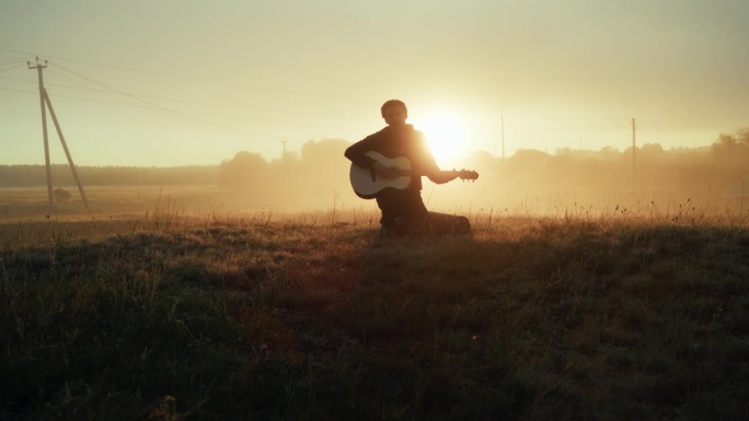 有艺术气息的人在电影般的雾日落乡村野外唱着歌，弹着原声吉他