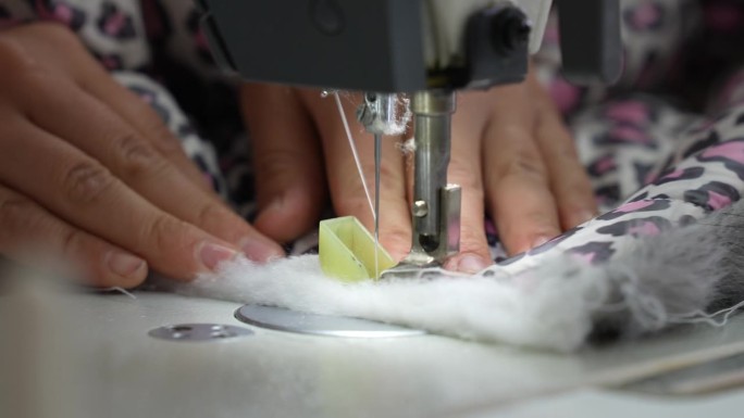 一只女工的手把布料推过缝纫机
