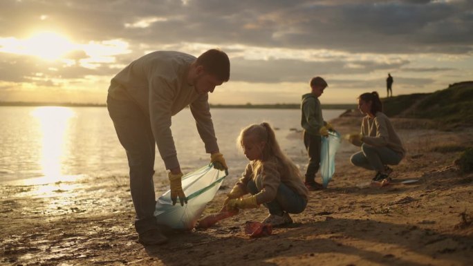 成人和儿童志愿者清理河岸的塑料垃圾，小女孩和父亲