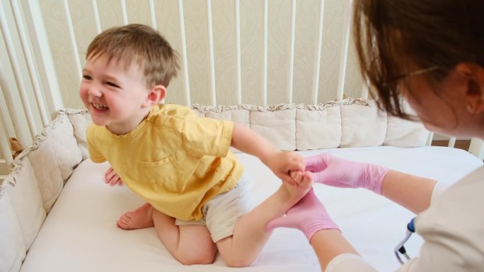 医生给蹒跚学步的婴儿做体操和足底按摩。穿制服的护士正在给孩子做腿部矫形练习。2岁左右(1岁11个月)