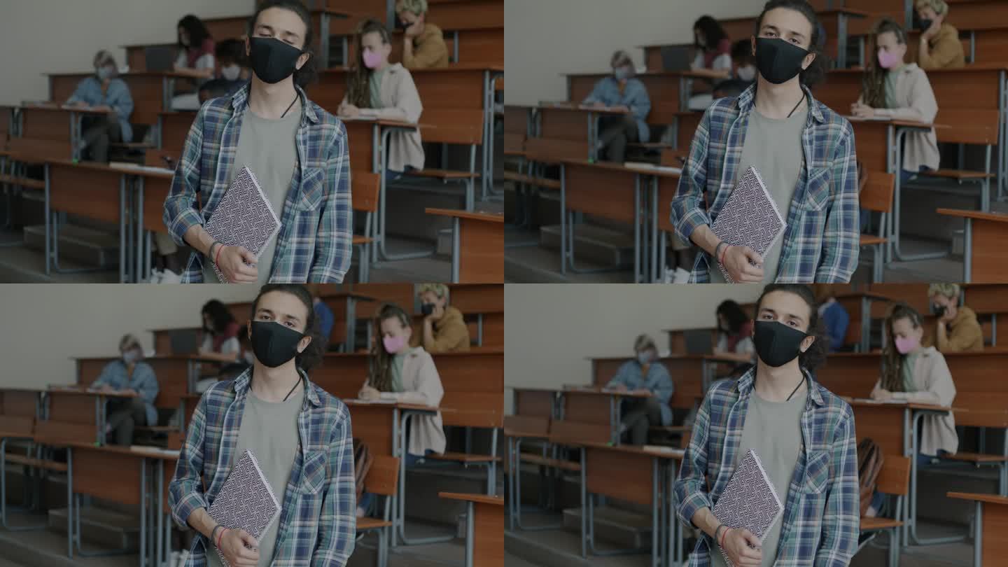 一名年轻大学生站在教室里，戴着医用口罩预防covid-19感染
