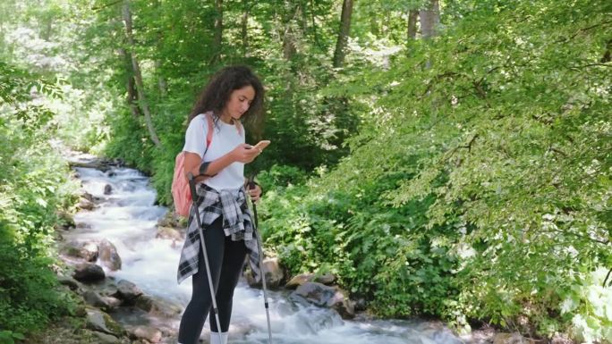 徒步旅行的女孩在地图上看智能手机，在河边的山上徒步旅行。