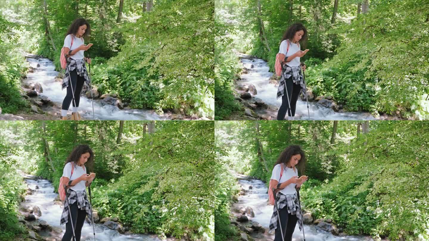 徒步旅行的女孩在地图上看智能手机，在河边的山上徒步旅行。