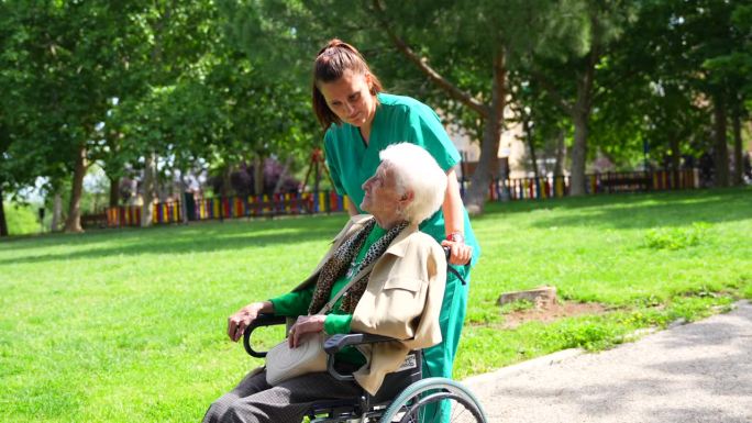 一位老年妇女和护士坐在轮椅上穿过养老院的花园，旁边是大自然和树木