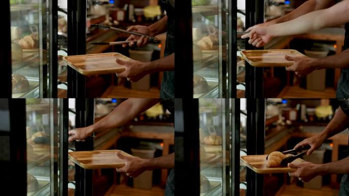 特写，亚洲男子双手拿着夹子，在开门之前，男子从装有许多面包店的橱柜里拿起糕点准备早餐，欢迎顾客，填饱