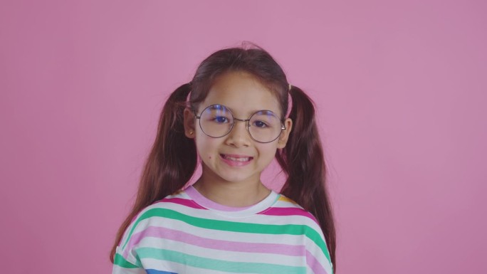 可爱的女孩戴着粉红色背景的眼镜。