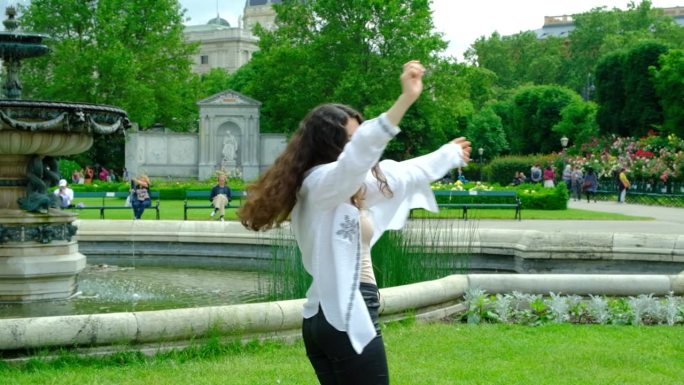 美丽的黑发女子在夏天的公园里高举双手旋转着自己。