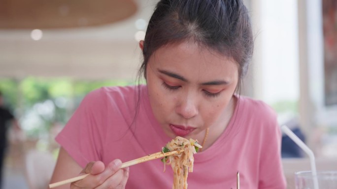 亚洲妇女在餐馆用筷子在碗里吃面条的特写。