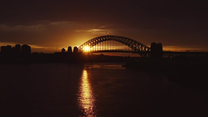 在金色的冬日日出中，宽镜头拍摄了悉尼海港大桥的背光剪影