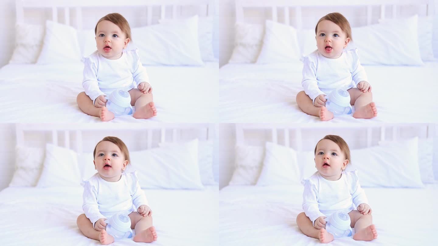 逗趣的六个月女婴穿着白色的衣服躺在床上笑着，拍着手，一个小孩子躺在家里的棉质床上，早上醒来后熟睡，概