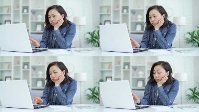 劳累过度的亚洲女商人厌倦了坐在家里办公室用笔记本电脑工作。困倦的女人无法集中精力工作