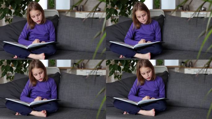 一个可爱的金发小女孩正坐在客厅的沙发上读一本彩色的大书。低龄学童自学，在家阅读文学作品，趣味休闲