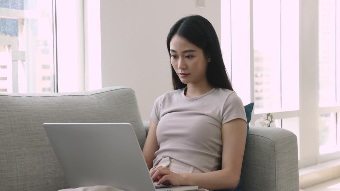 亚洲自由职业女孩坐在沙发上用笔记本电脑工作