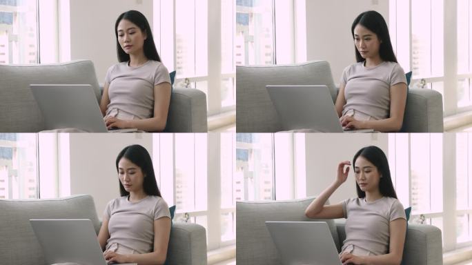 亚洲自由职业女孩坐在沙发上用笔记本电脑工作