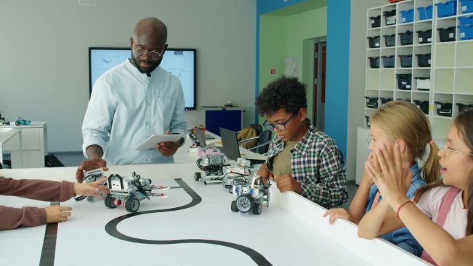 不同的孩子和老师看着电动机器人在桌子上移动