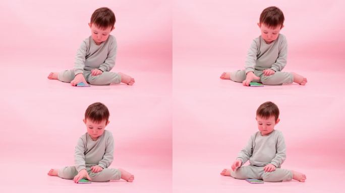 快乐的蹒跚学步的婴儿与手机工作室粉红色的背景。小男孩手里拿着智能手机。孩子一岁八个月，身高正常