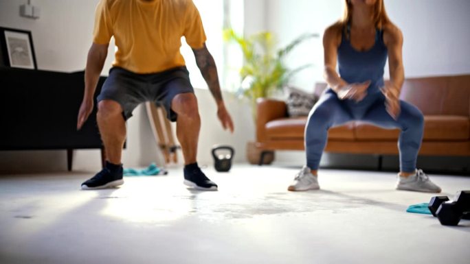 慢动作健身年轻夫妇做跳深蹲在家锻炼，一起在客厅锻炼。力量,健康,活力,健康的生活方式。以8K分辨率拍