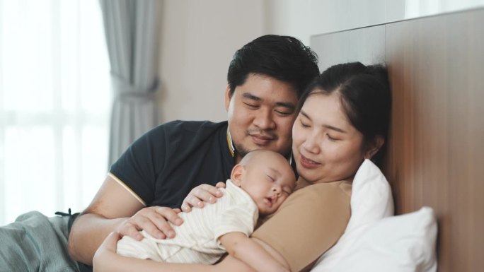 一对亚洲父母抱着刚出生的儿子，哄他在家里的卧室里睡觉。母亲和孩子之间的关系