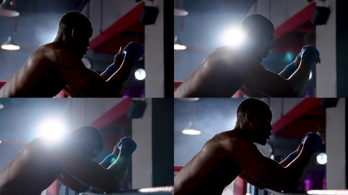 非洲拳击手不穿t恤，露出强壮的肌肉，站在拳击台上的角落里沉思，准备与对手较量，争取胜利
