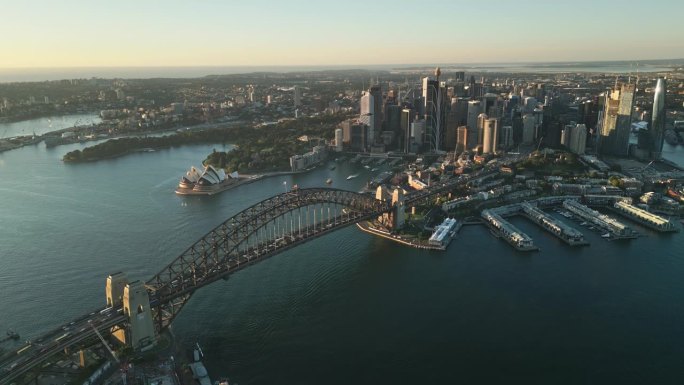 澳大利亚新南威尔士州悉尼日出时，悉尼港大桥、各种办公大楼和歌剧院上空的4K鸟瞰图