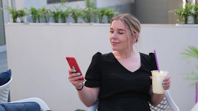 一个漂亮的女人坐在街边的咖啡馆里打电话。咖啡厅里的女性一边喝着饮料，一边上网。