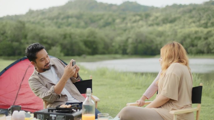 亚洲父亲在度假露营野餐时，用手机为家人在户外拍照。