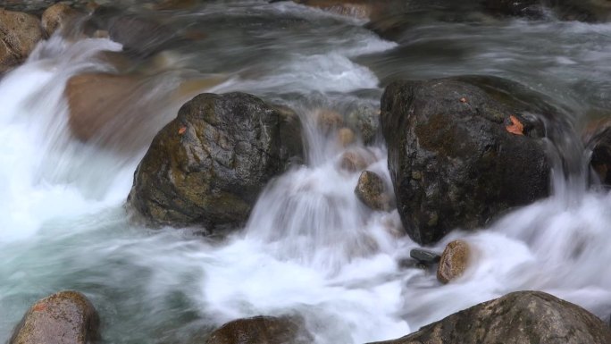 用低快门技术在河床上的大圆形椭圆形岩石之间流动的泡沫水流