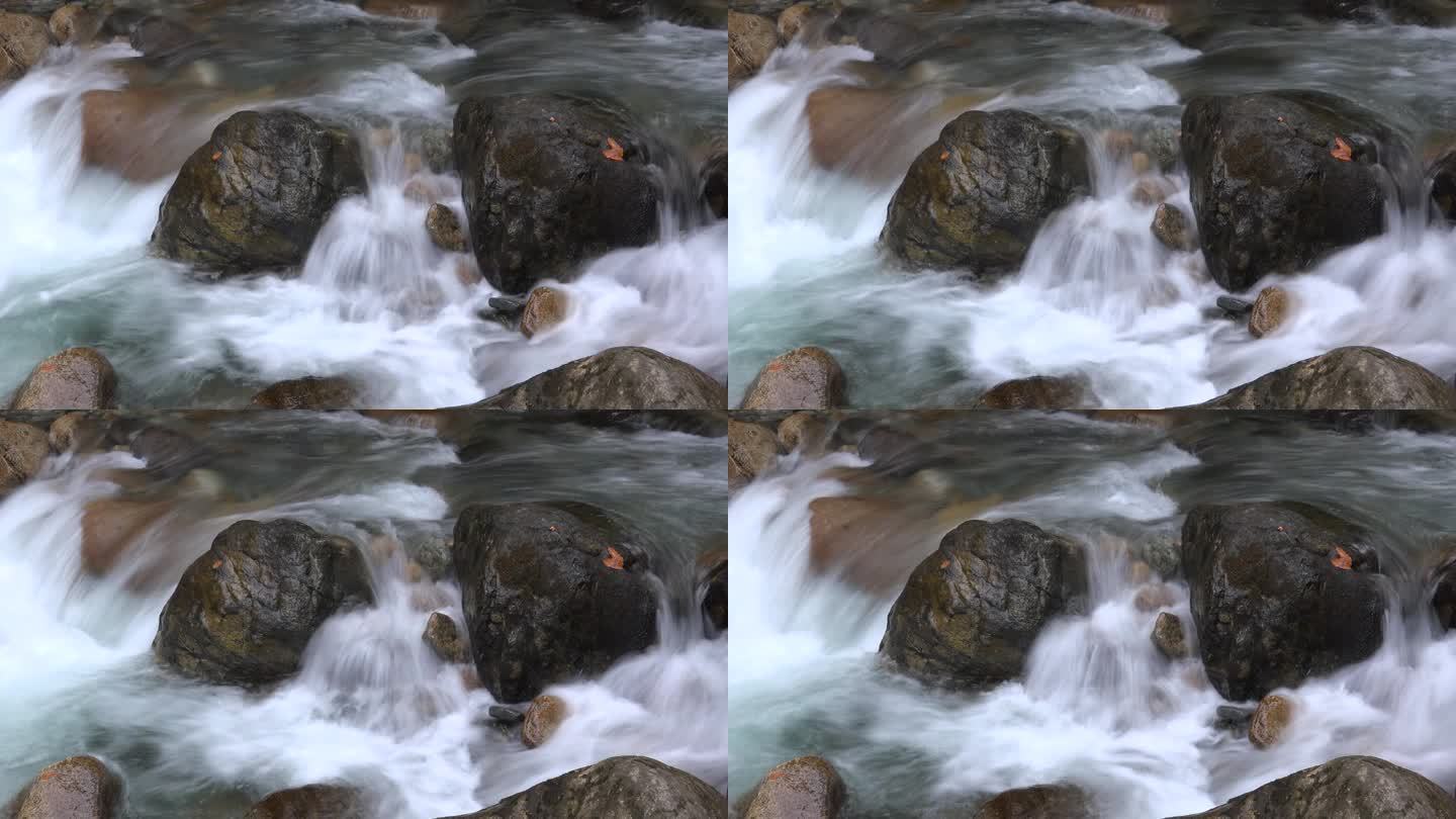 用低快门技术在河床上的大圆形椭圆形岩石之间流动的泡沫水流