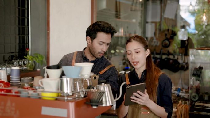 亚洲夫妇共同创造了这家咖啡馆，女人从顾客那里订购食物和饮料，男人借用点餐机为顾客点咖啡，穿着围裙保持