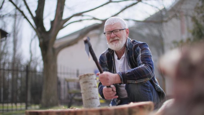 伐木工，一个戴着眼镜、留着胡子和头发的老人，正在用斧头把坐在街上的树砍成树桩