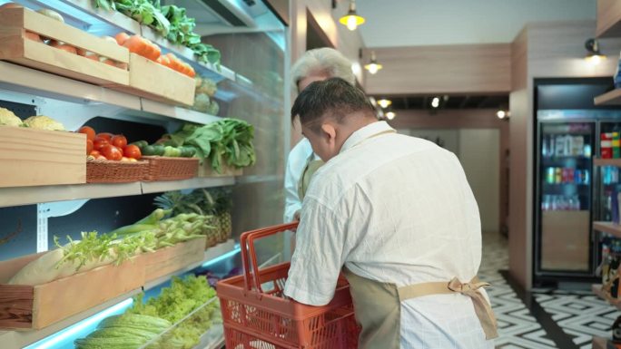 患有唐氏综合症的年轻亚洲男子和他的资深女同事站在冰箱前采摘蔬菜和食品，然后送到顾客家。残疾超市。
