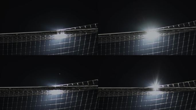 在晚上的足球比赛中，球门横梁与球网背面。英式足球比赛。体育场聚光灯下的照明弹和灯光。体育的概念。近距