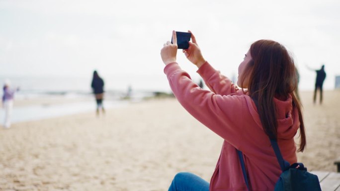 妇女用手机发短信和照片享受放松在布莱顿海滩五颜六色的房子