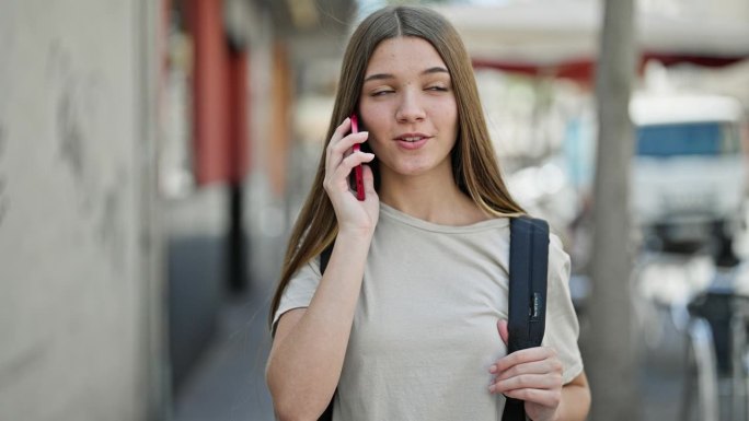 年轻漂亮的女学生背着双肩包在街上讲智能手机