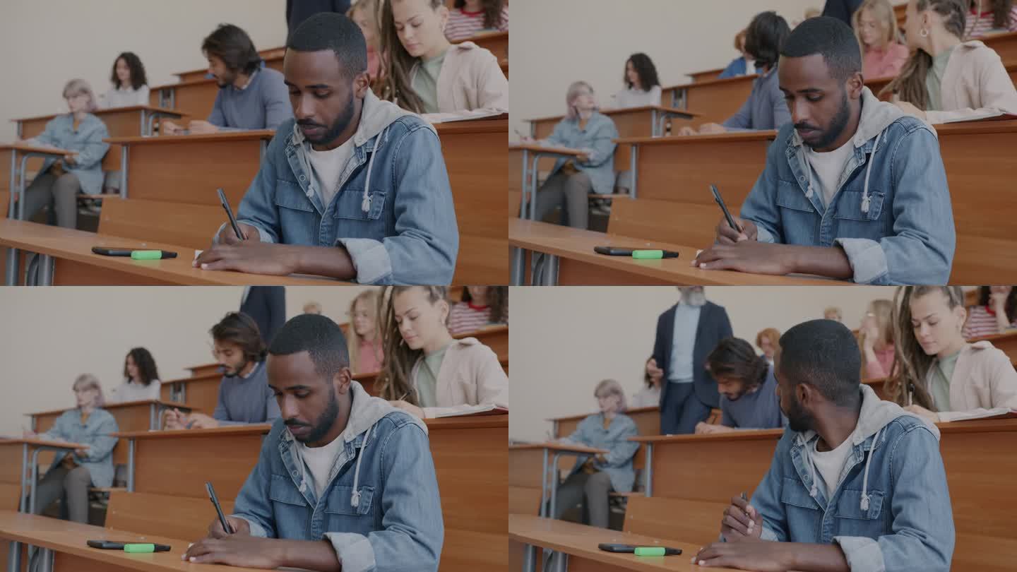 年轻的非裔美国男学生听大学老师讲课并在课堂上写信息