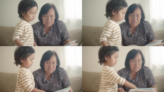 亚洲老妇人拿着一本书，她的孙子指着书页，孙子一边看书一边说话。