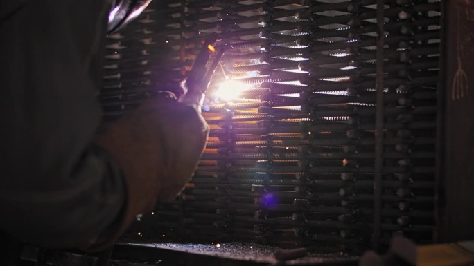 焊工在建筑工地为整体工程焊接金属棒的焊工。焊接产生火花和烟雾。