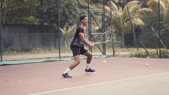 一名亚裔马来少年在网球场打网球友谊赛