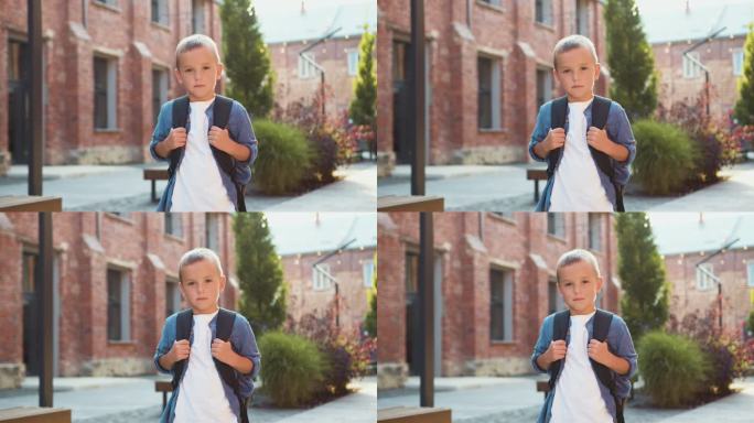 小男孩背着双肩包站在校园里望着镜头的照片。肖像快乐的孩子。换一个校园。肖像快乐的学生。