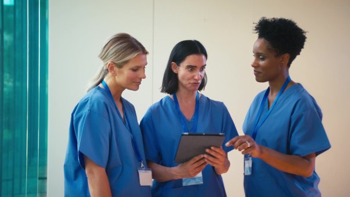 三个成熟的女医生穿着手术服拿着电子平板电脑在医院讨论病人的记录