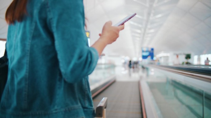 在机场，一名女子拿着登机牌走到登机口，查看智能手机