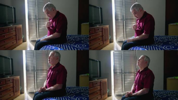 一位虔诚的天主教老人坐在家里的床边做十字架祈祷。有感恩和信仰的精神上的人