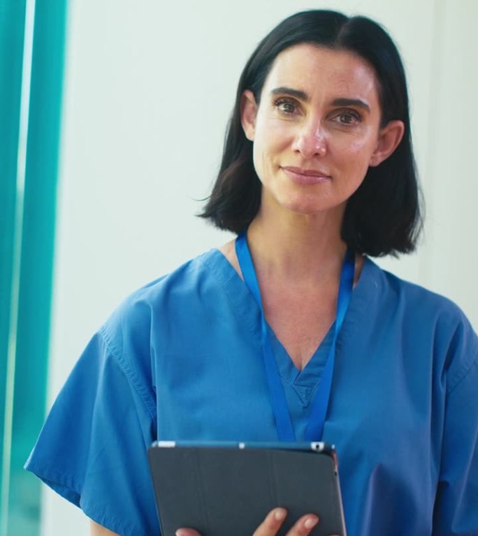 成熟女医生的垂直视频肖像在医院里穿着手术服和数字平板电脑