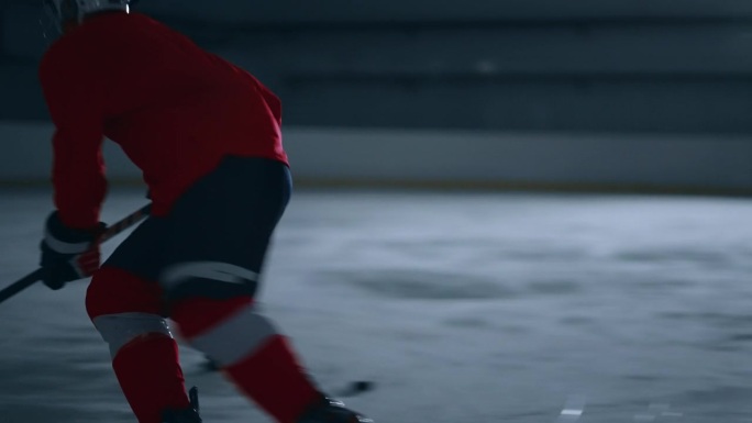 一名身穿红色球衣的冰球高手在黑暗的冰场上展示了他令人印象深刻的技术，同时避开了障碍，并精确地得分