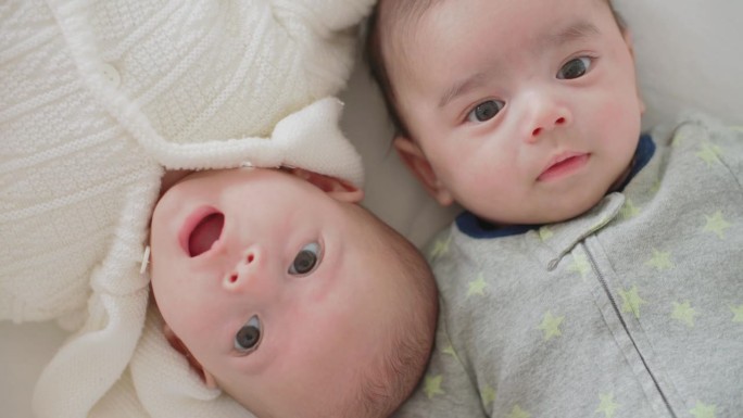 可爱的刚出生的双胞胎宝宝男孩和女孩一起躺在家里的床上。