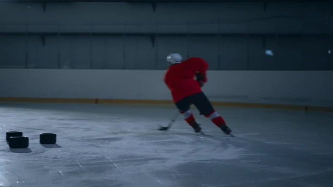 一名身穿红色球衣的冰球运动员在黑暗的冰场上展示着他令人难以置信的敏捷和速度
