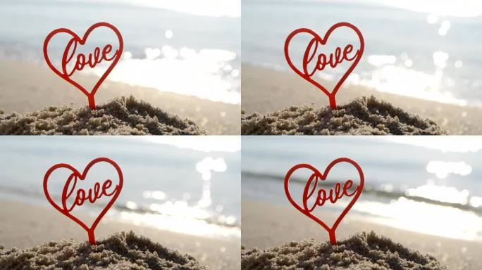 塑料棒形状的红色心脏和文字的爱在沙滩沙滩沙滩上，在阳光明媚的夏日海滨特写。人物形状的心字爱的背景海浪