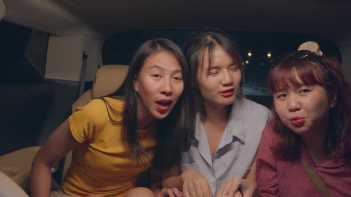 一群年轻的亚洲朋友在晚上开着车在城市里兜风去度假。汽车旅游目的地。